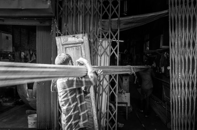 Man carrying long wooden beams through alleyway